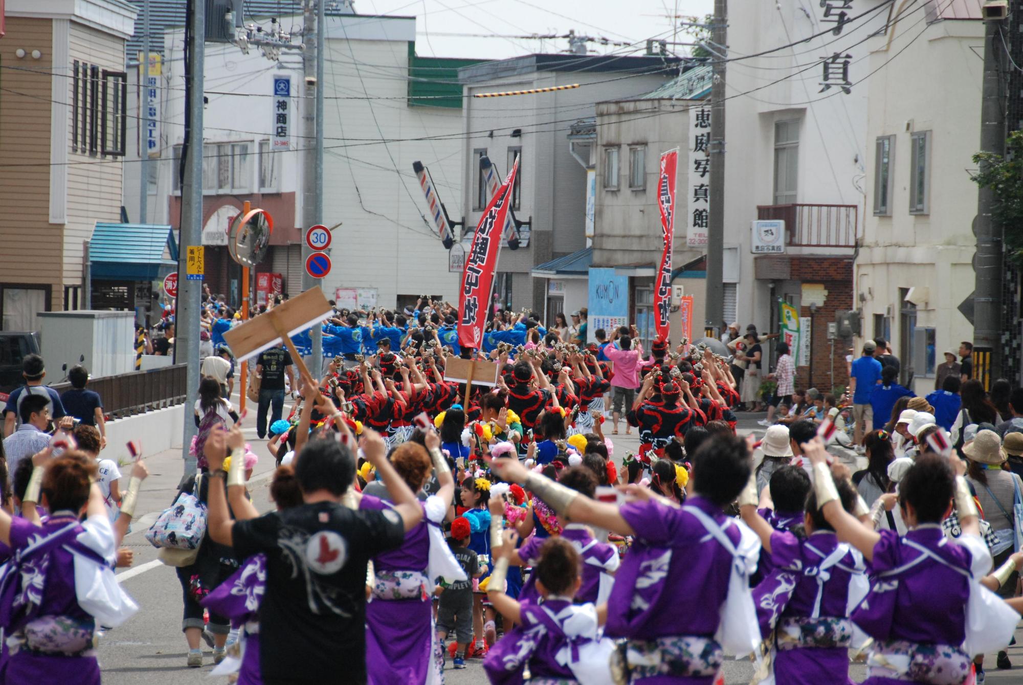 紫色と白色の柄をした衣装を着てすずらん踊りを踊る人たちの写真