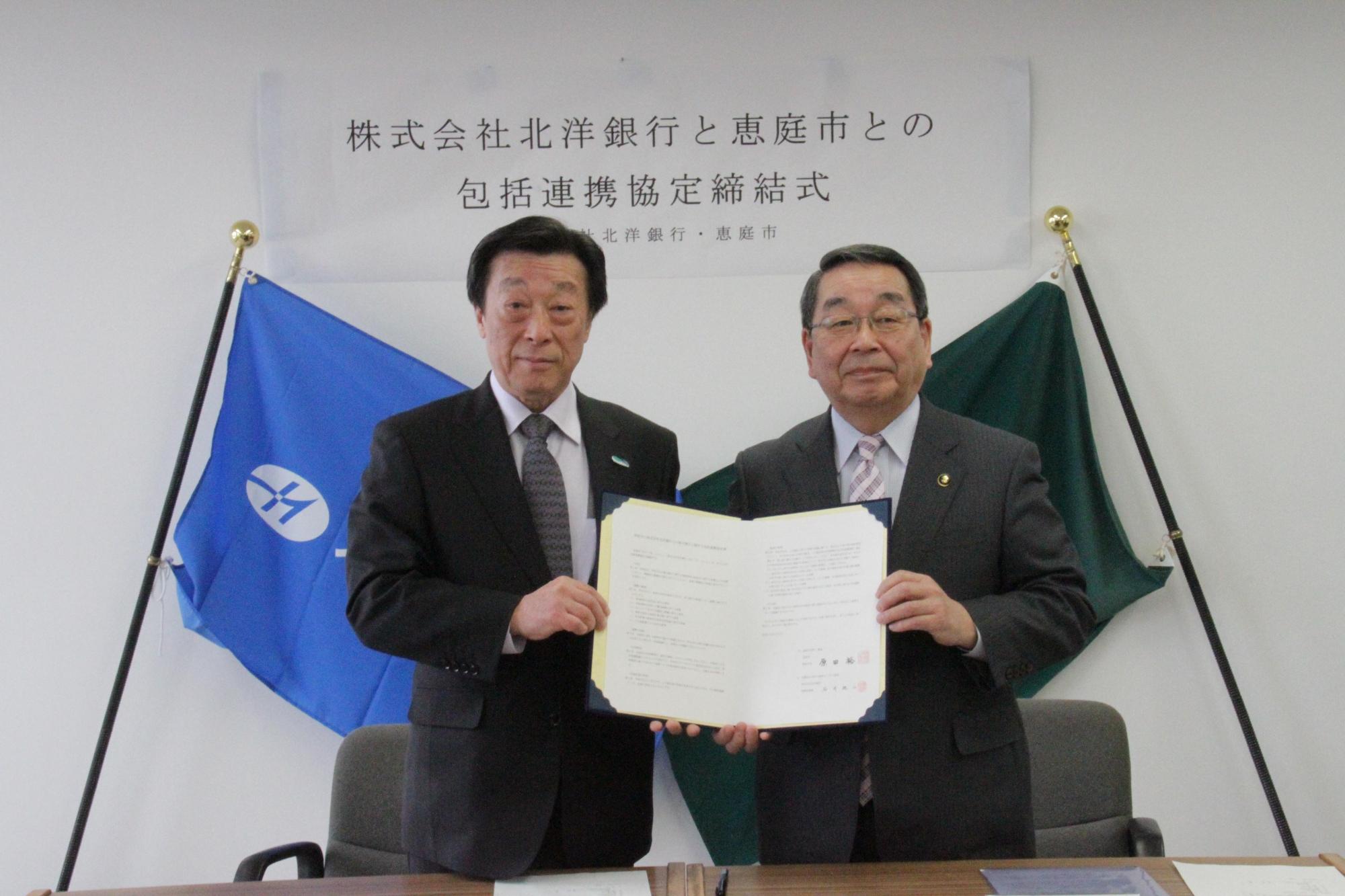 包括連携協定締結式にて北洋銀行の石井純二氏と恵庭市長の原田裕氏が包括連携協定書を持っている写真