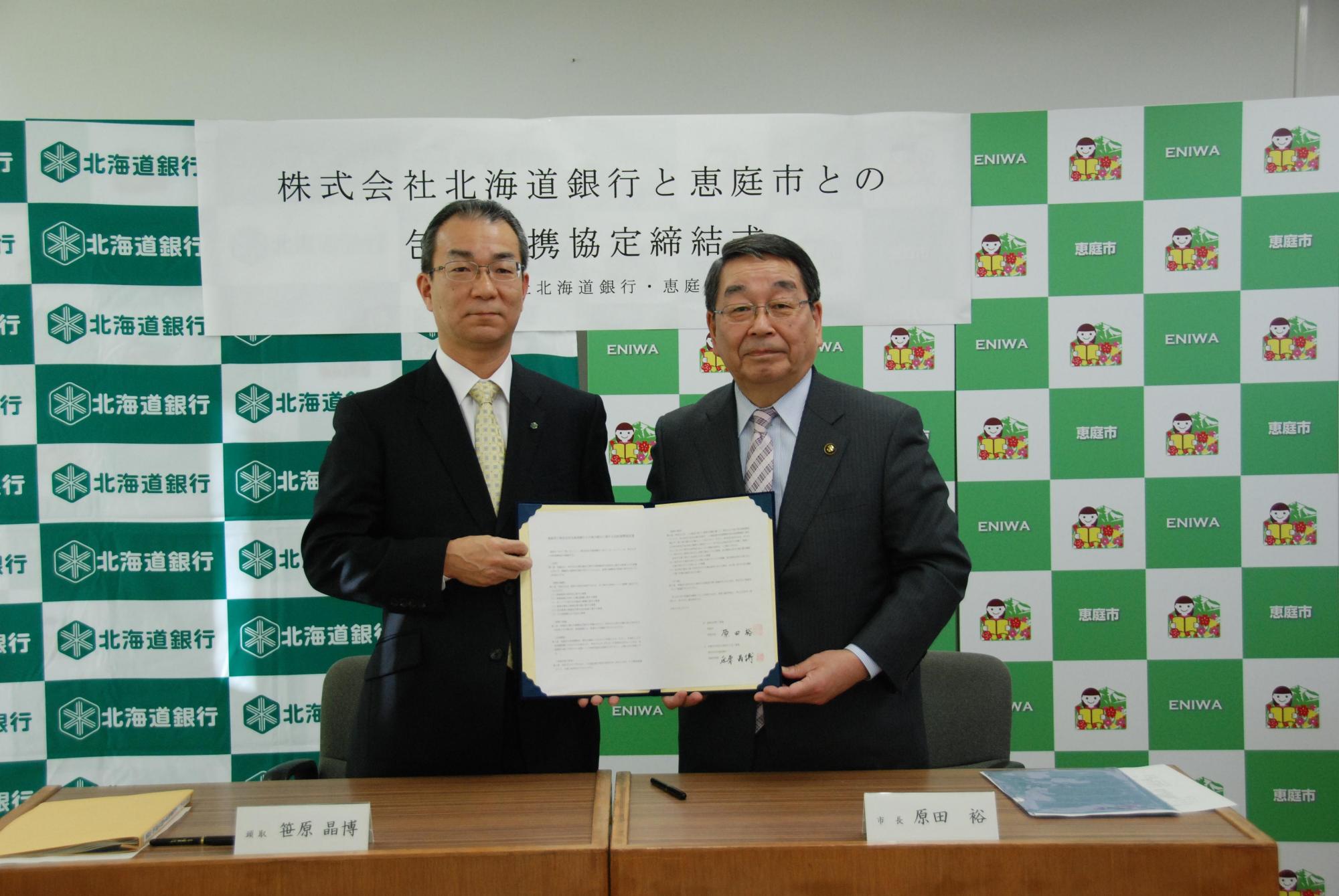 包括連携協定締結式にて北海道銀行の笠原晶博氏と恵庭市長の原田裕氏が包括連携協定書を持っている写真