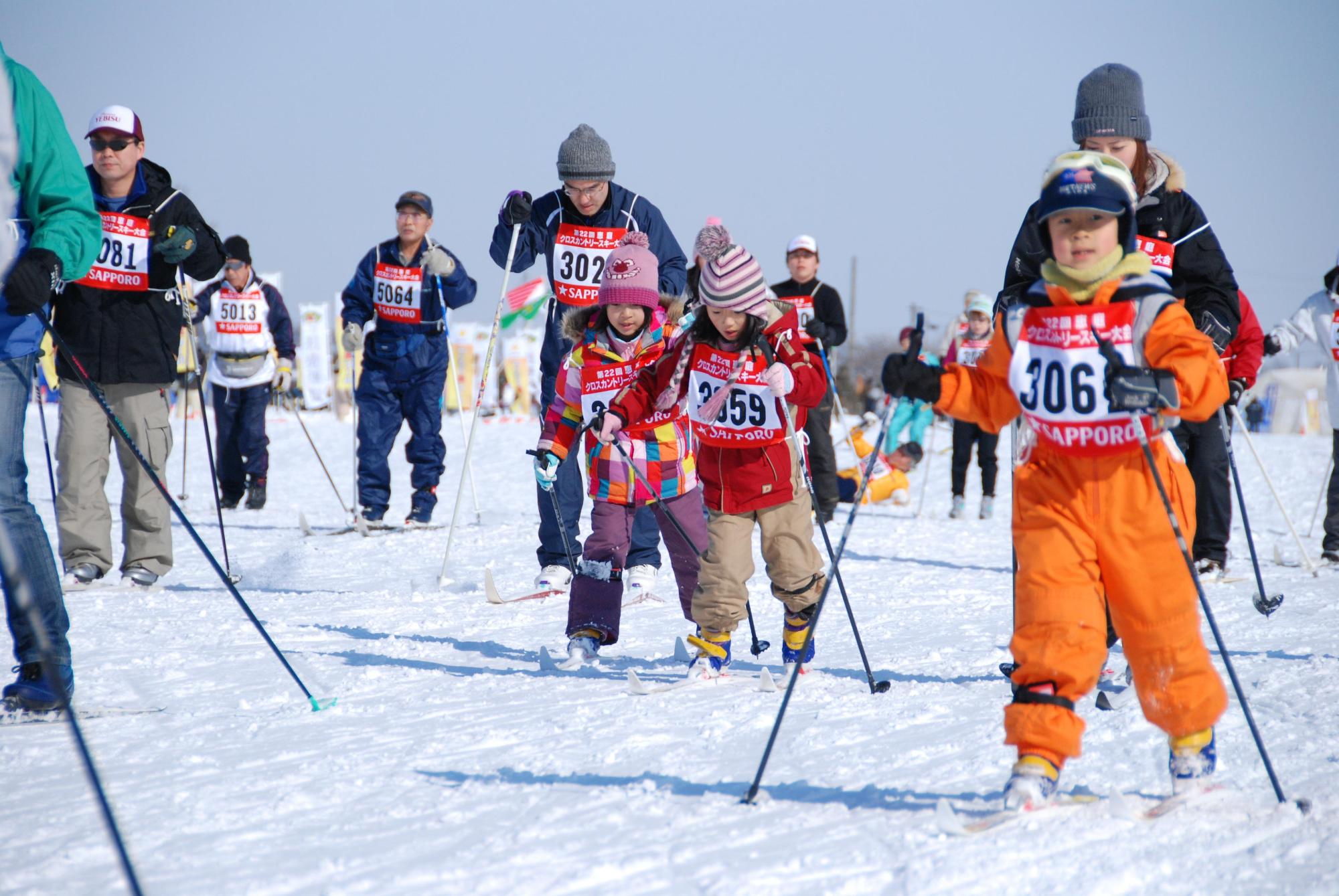 雪の上で子供から大人までの多くの人がスキーをしている写真