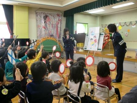 交通安全児童指導員の方が紙芝居を使いクイズを出し、マルかバツかの札をあげている幼稚園児の写真