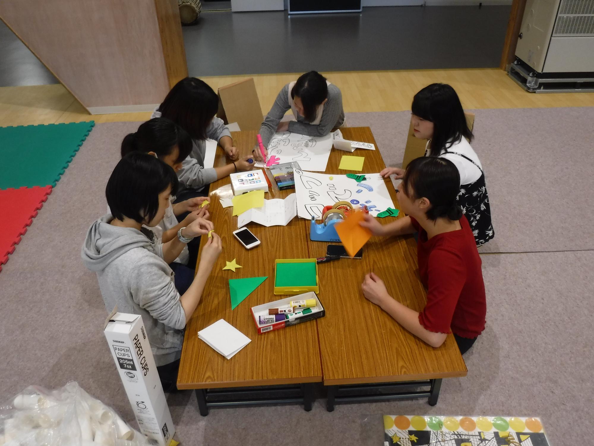 6人の女の子がテーブルの周りに座って折り紙をしている写真
