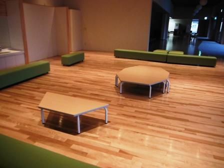 夕方に撮られた八角形や台形のテーブルと緑色のソファーが設置されたプレイスペースの写真