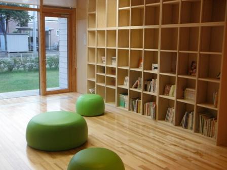 本棚の前に緑色の丸いクッションが3つ並んで設置されている子ども図書コーナーの写真