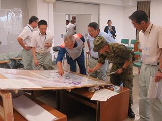 市役所にて行われた災害対策本部訓練にて職員と自衛隊員と共に地図を確認する原田市長の写真