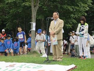 芝生の上に設置されたスタンドマイクの前で挨拶をする原田市長の写真