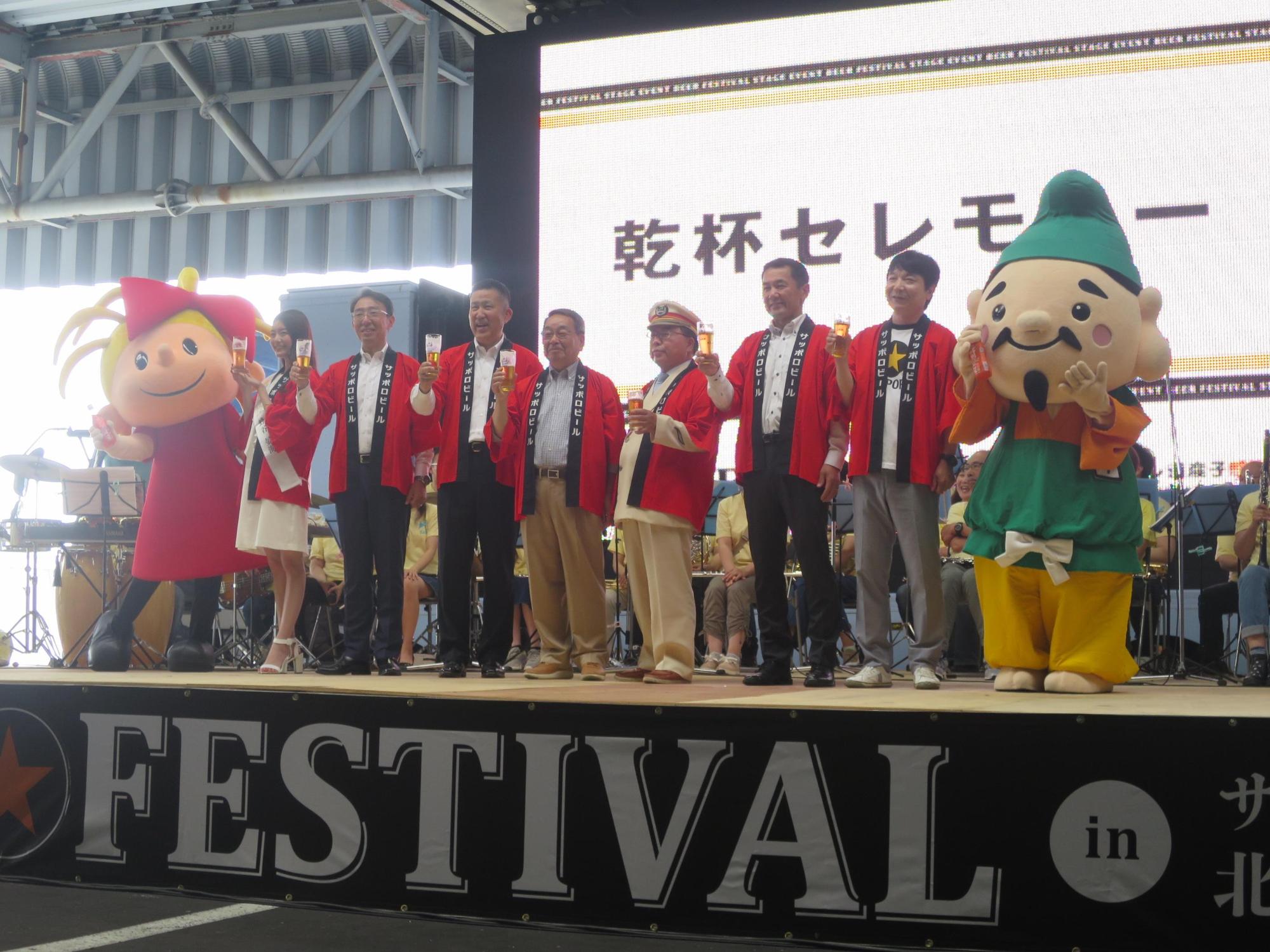 おんこ祭のステージでビールを片手に並ぶ原田市長と関係者の写真