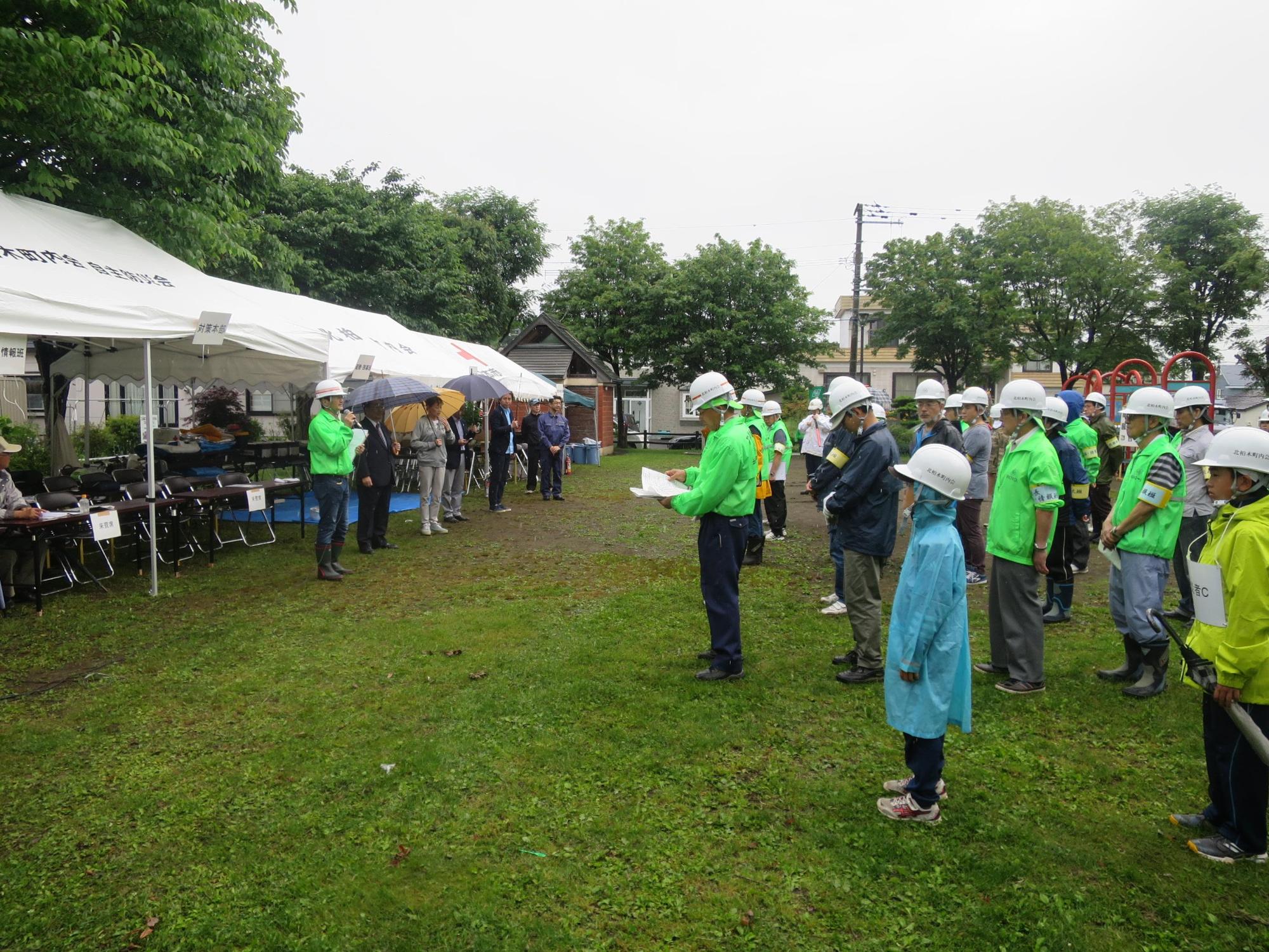 雨の中、傘を差しながら挨拶をする原田市長と雨具を着た参加者らの写真
