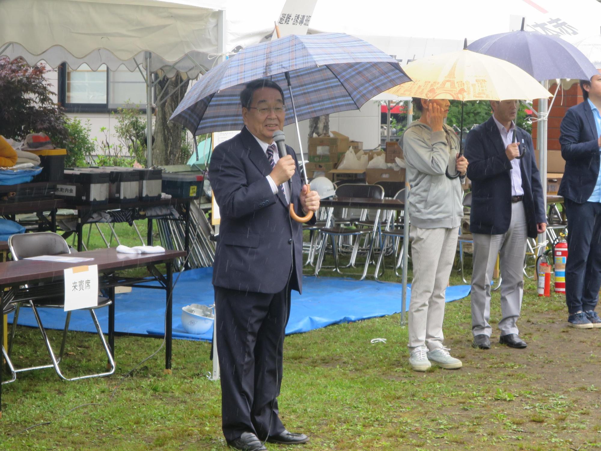 雨の中、傘を差しながら挨拶をする原田市長の写真