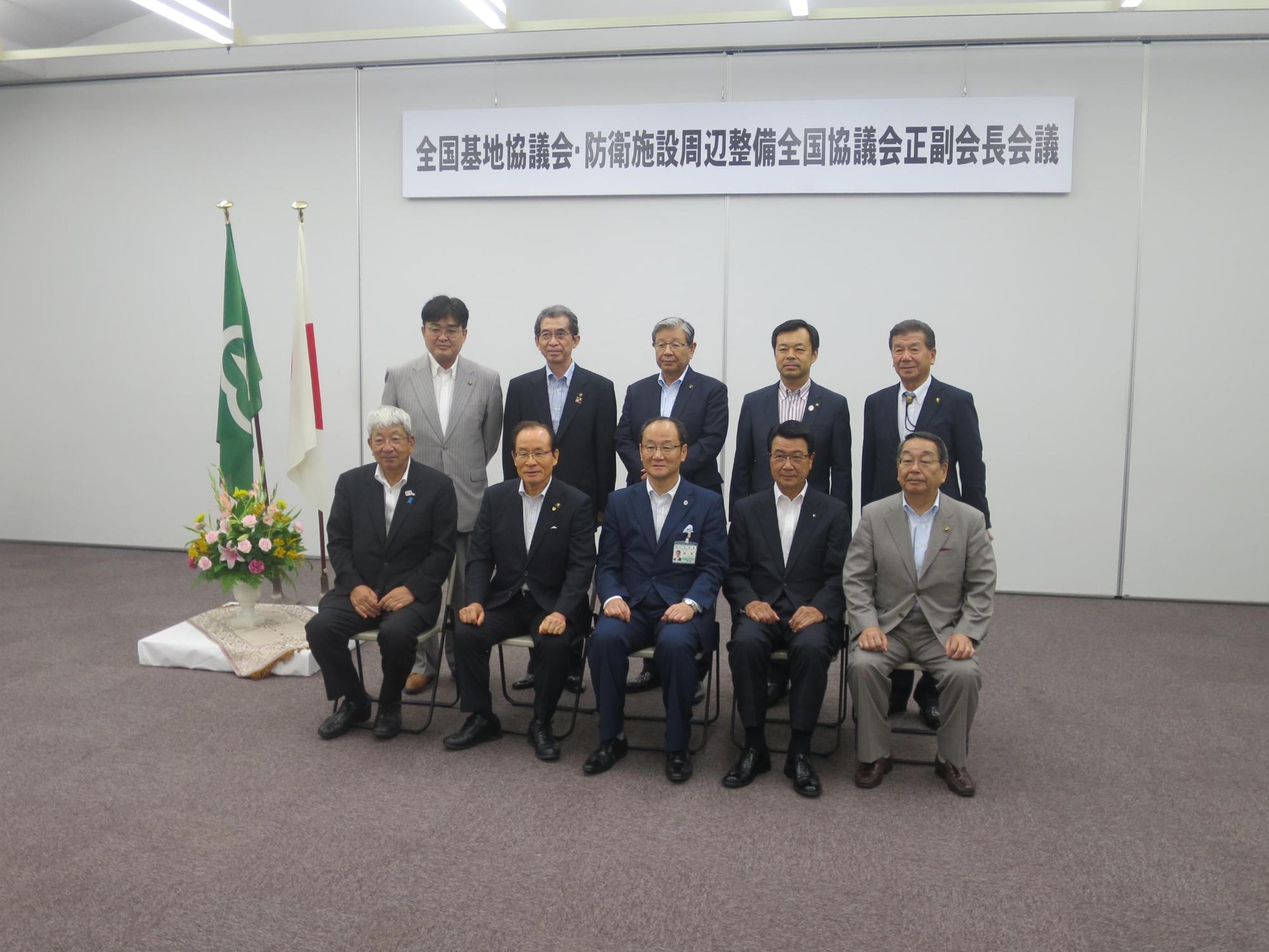 会議名のパネルの前に並ぶ原田市長と会議出席者らの写真