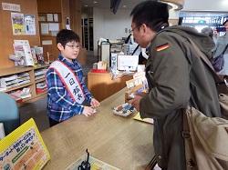 一日館長を務める小学生がカウンター越しに、本を借りに来た男性の対応に務めている写真